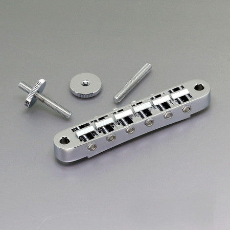 Silver metal ABR-style guitar bridge with two screws and a thumbwheel nut on gray background.