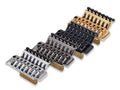 Four guitar locking tremolo bridges in silver, black, dark gray, and gold finishes displayed in a row.