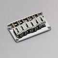 A silver metal guitar hardtail bridge with six adjustable saddles on a gray background.