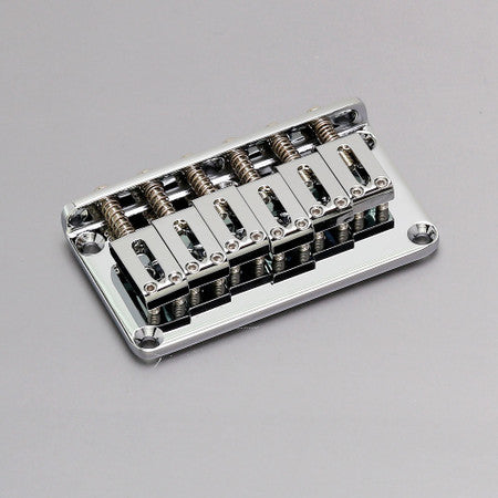 A silver metal guitar hardtail bridge with six adjustable saddles on a gray background.