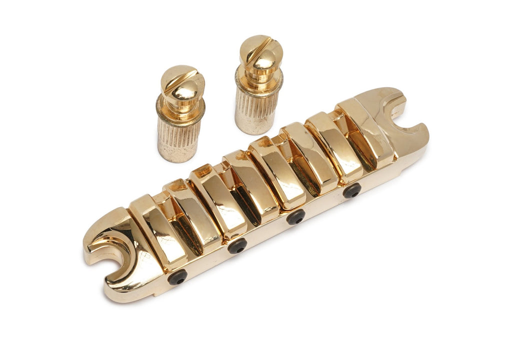 Gold-colored guitar or bass bridge piece with two cylindrical mounting posts.