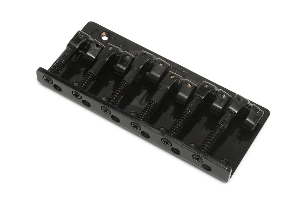 A black metal bridge with six adjustable saddles for strings, likely for a bass guitar.