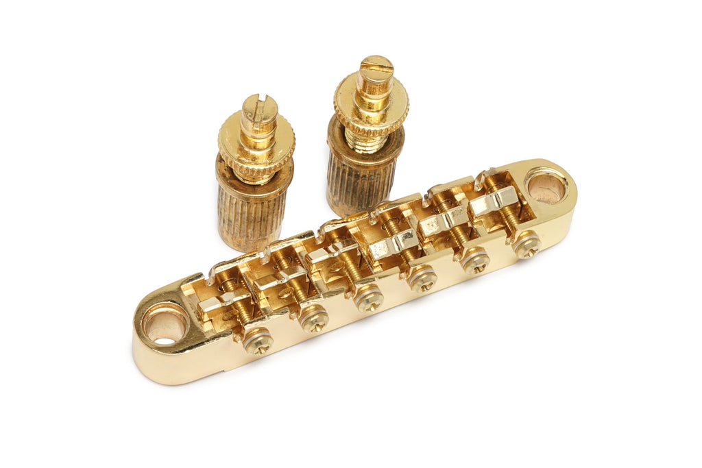 Gold tune-o-matic style guitar bridge with two thumbwheels on a white background