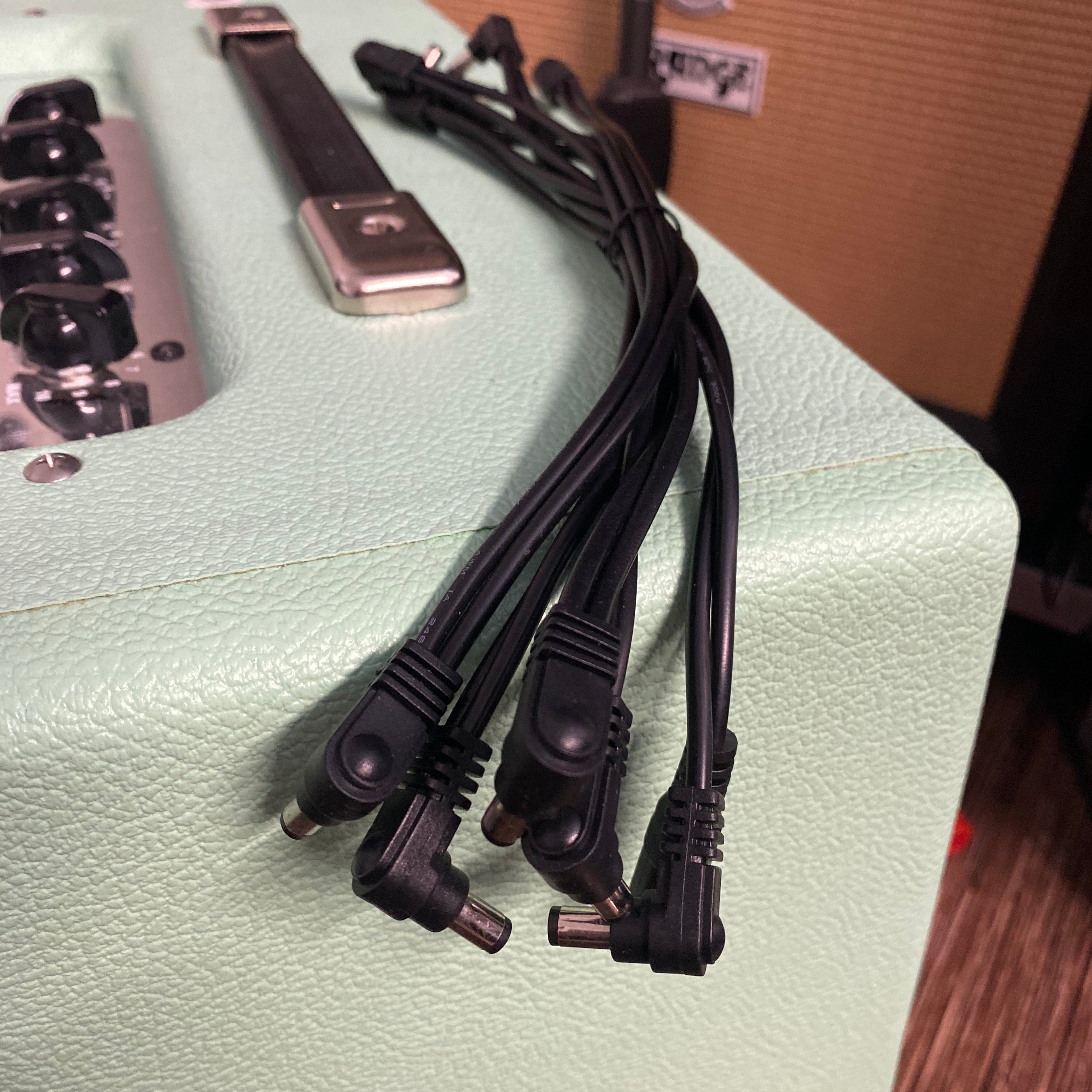 Black daisy-chain power cable with barrel connectors on a light green textured surface near a control panel.