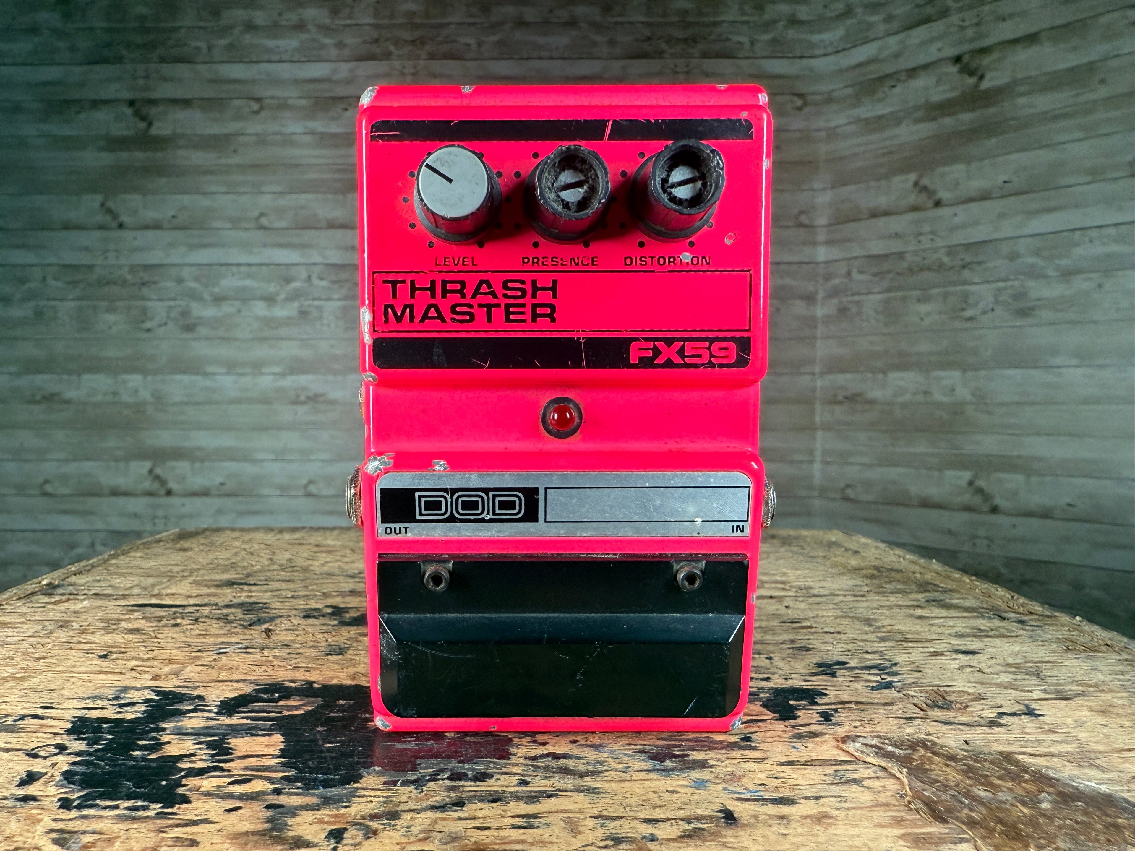 Red DOD Thrash Master FX59 guitar effects pedal with three control knobs on a wooden surface.