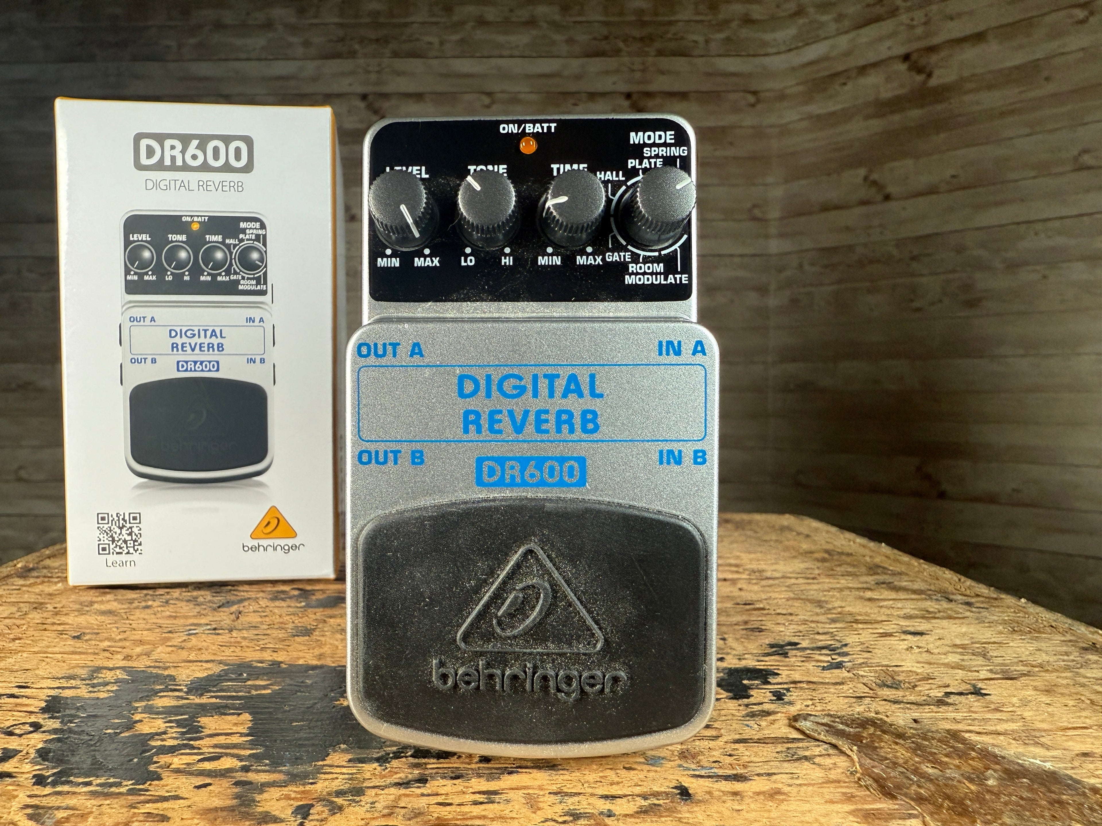 Behringer DR600 digital reverb pedal with four control knobs and box placed on wooden surface.