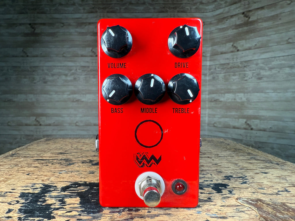 Red guitar effects pedal with five knobs, footswitch, and a small red LED indicator on a wooden surface.