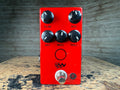 Red guitar effects pedal with five knobs, footswitch, and a small red LED indicator on a wooden surface.