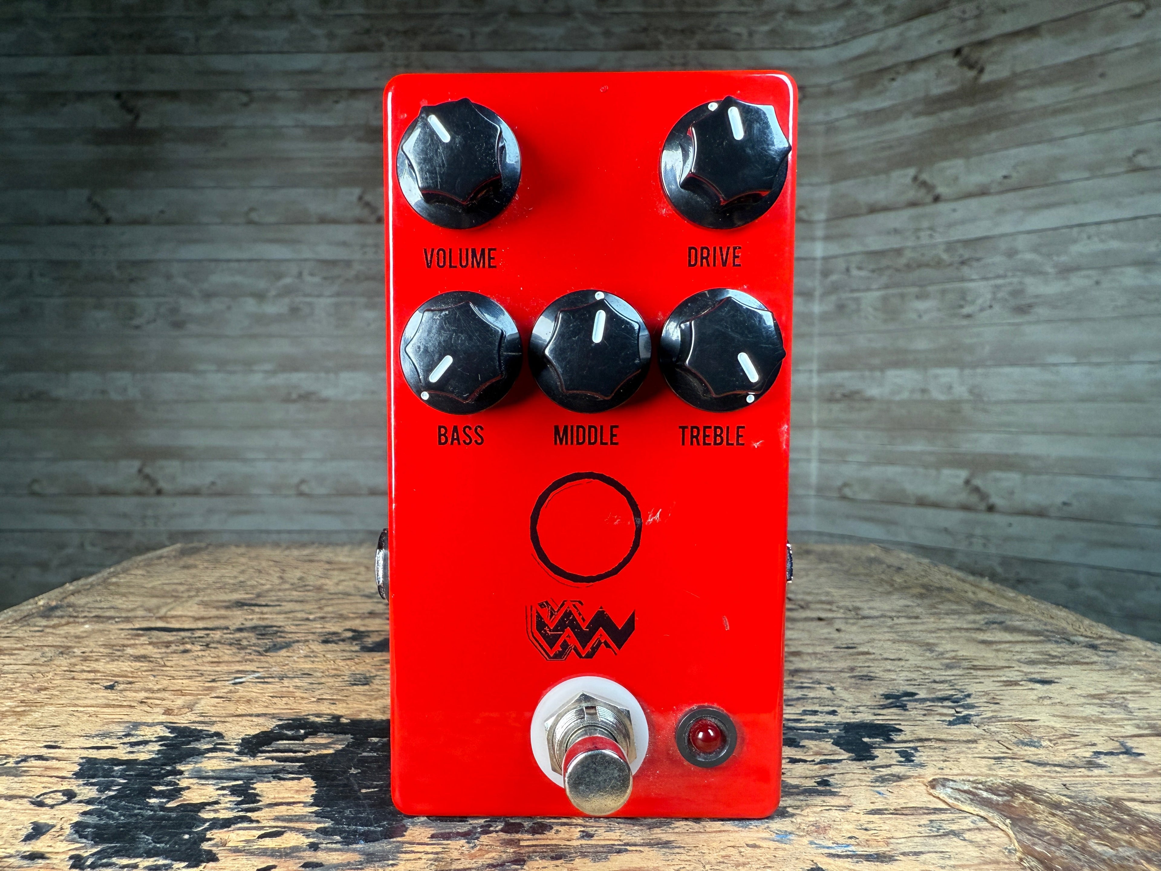Red guitar effects pedal with five knobs, footswitch, and a small red LED indicator on a wooden surface.
