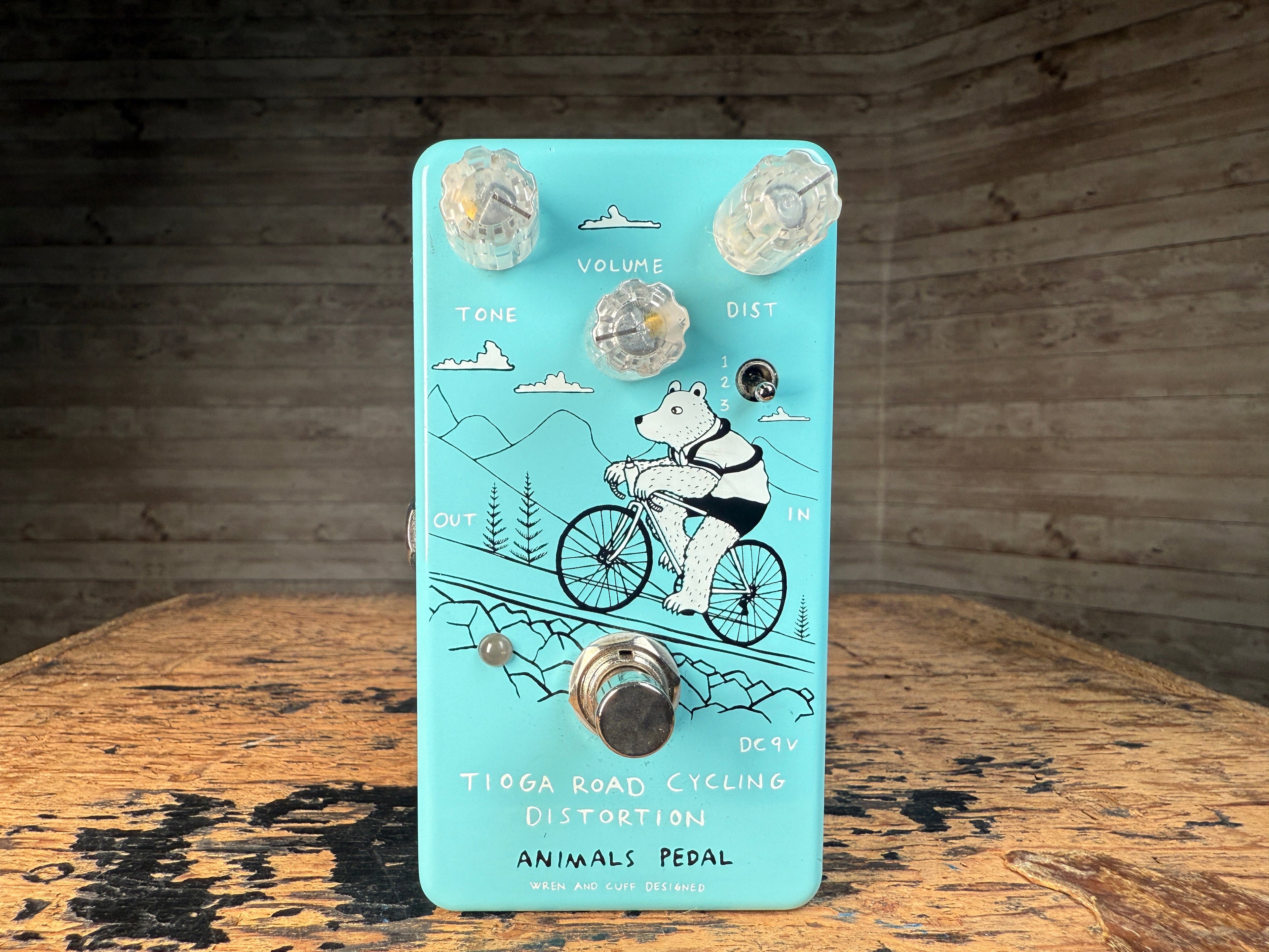Light blue guitar effects pedal with three knobs, one toggle switch, one footswitch, and a bear riding a bicycle illustration.