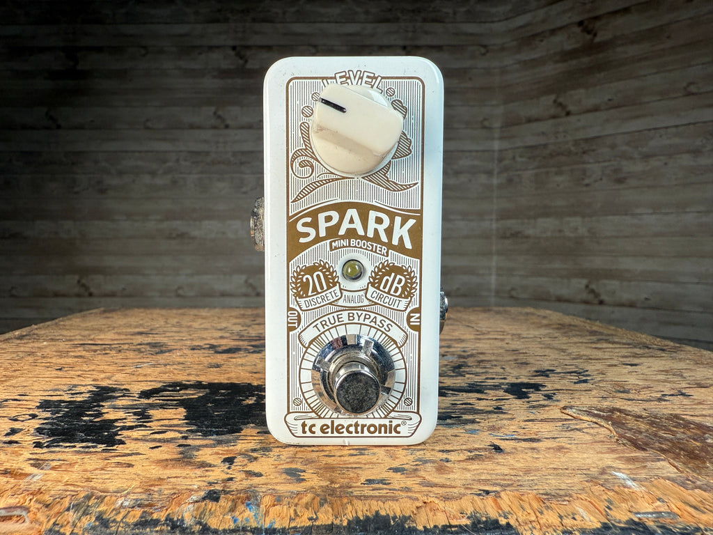 White TC Electronic Spark Mini Booster pedal with one knob, footswitch, and input/output jacks on a wooden surface.