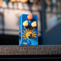 Blue guitar effects pedal with orange and yellow sun design and three control knobs labeled S, D, and L with a foot switch and visible input/output jacks.