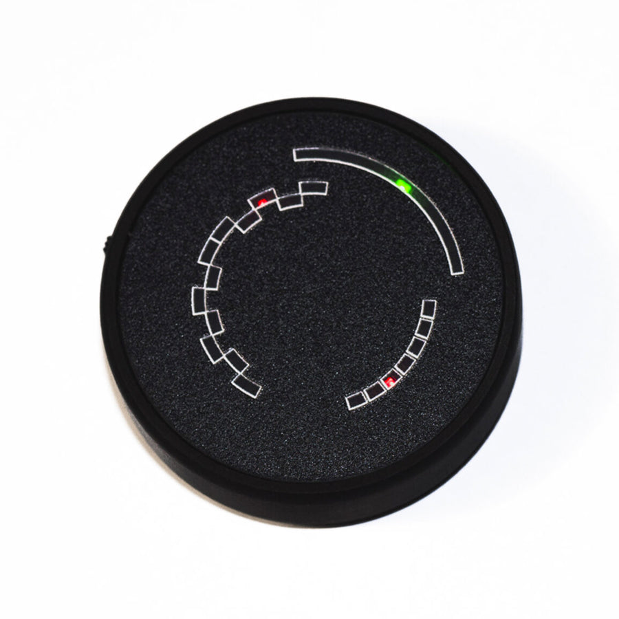 Round black tuner device with geometric dial markings and red and green LED indicators on front face.