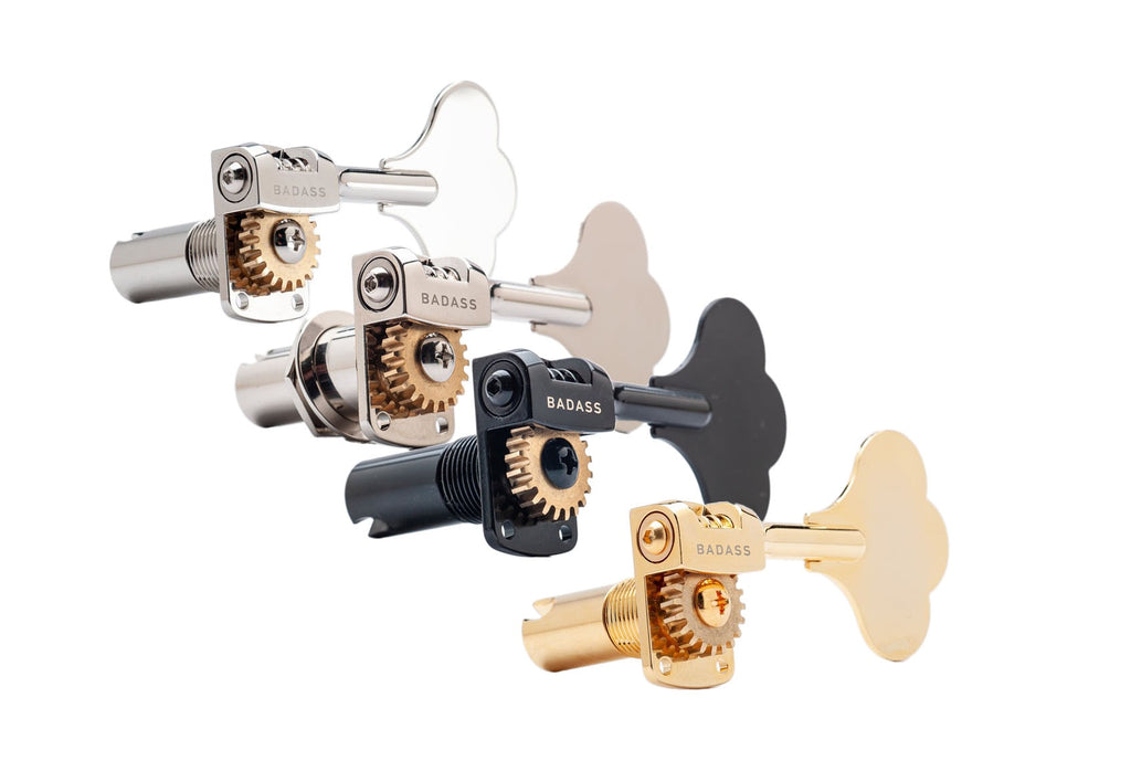 Four metal bass tuning keys with visible gears in silver, black, and gold finishes arranged in a row.
