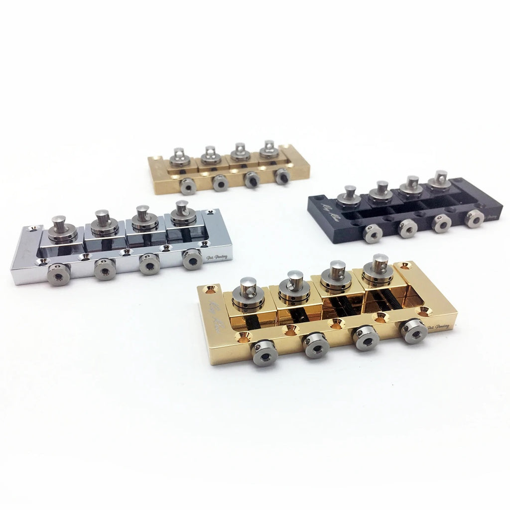 Four metal 4-string bass bridges in gold, silver, black, and brass finishes arranged on white background.