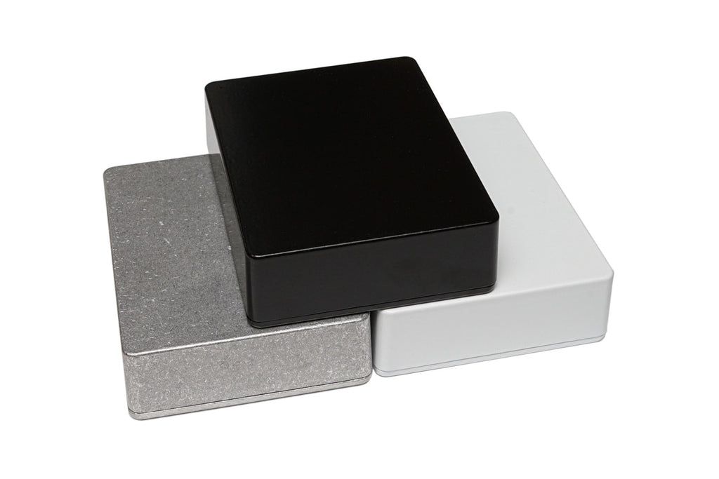 Three rectangular metal enclosures in black, white, and metallic gray stacked overlapping each other.