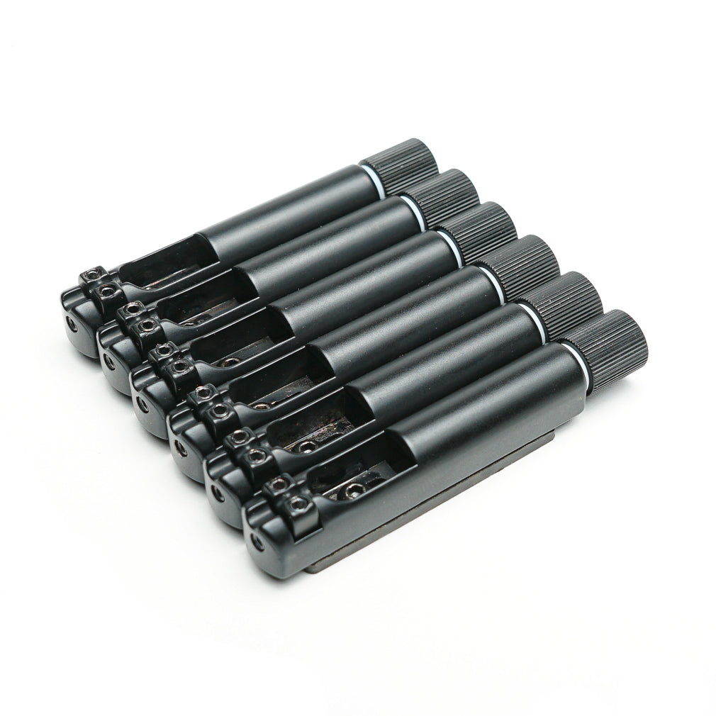 Set of six black cylindrical guitar bridge saddles with adjustment knobs arranged in a row.