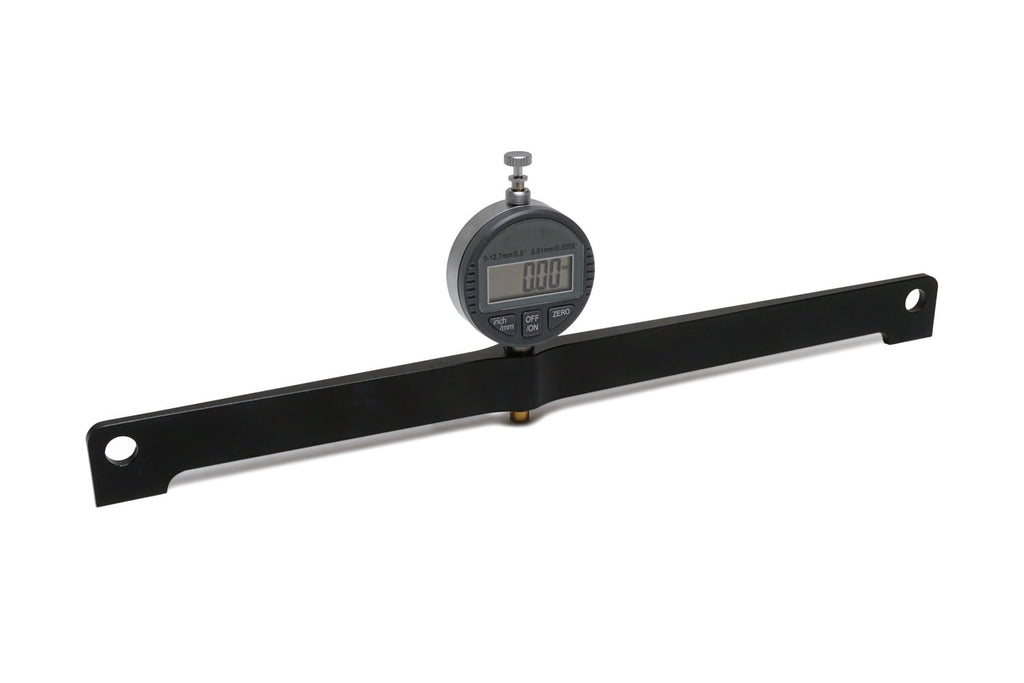 Digital dial gauge mounted on a black metal bar with holes on both ends against white background.
