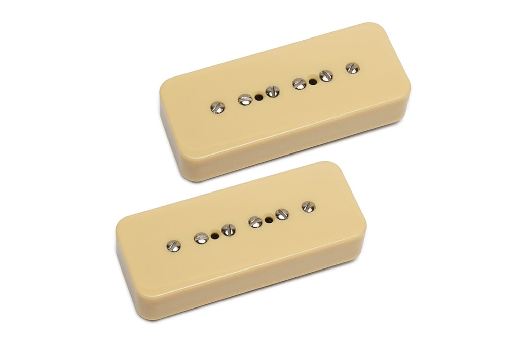 Two cream-colored P90 style guitar pickups with metal pole screws on a white background.