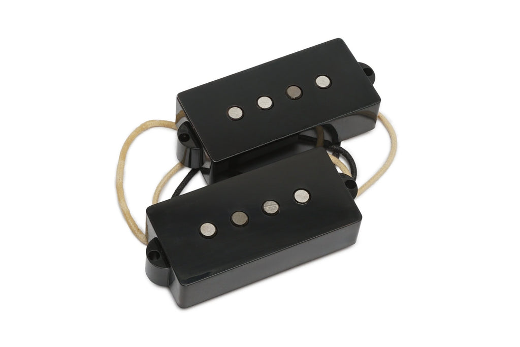Two black rectangular bass guitar pickups with four metal pole pieces and attached beige and black wires.