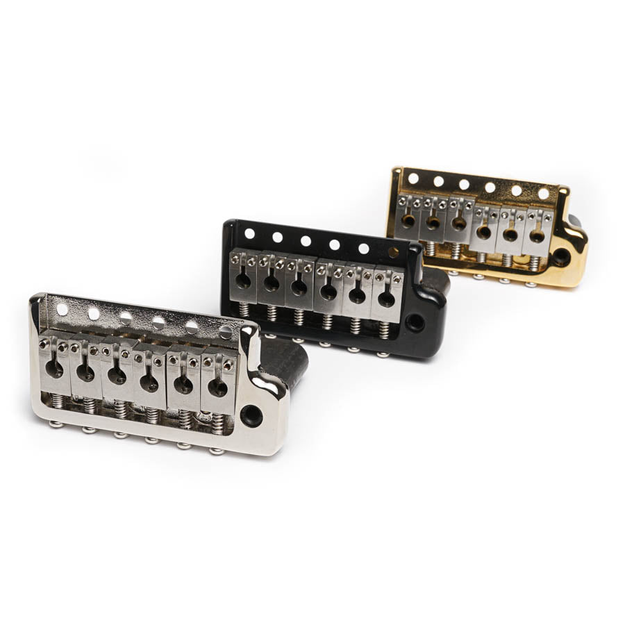 Three metal guitar bridges in silver, black, and gold finishes arranged in a diagonal line on a white background.