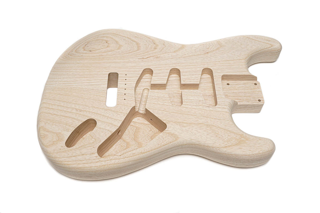 Unfinished light brown wooden guitar body carved with pickup and control cavities.