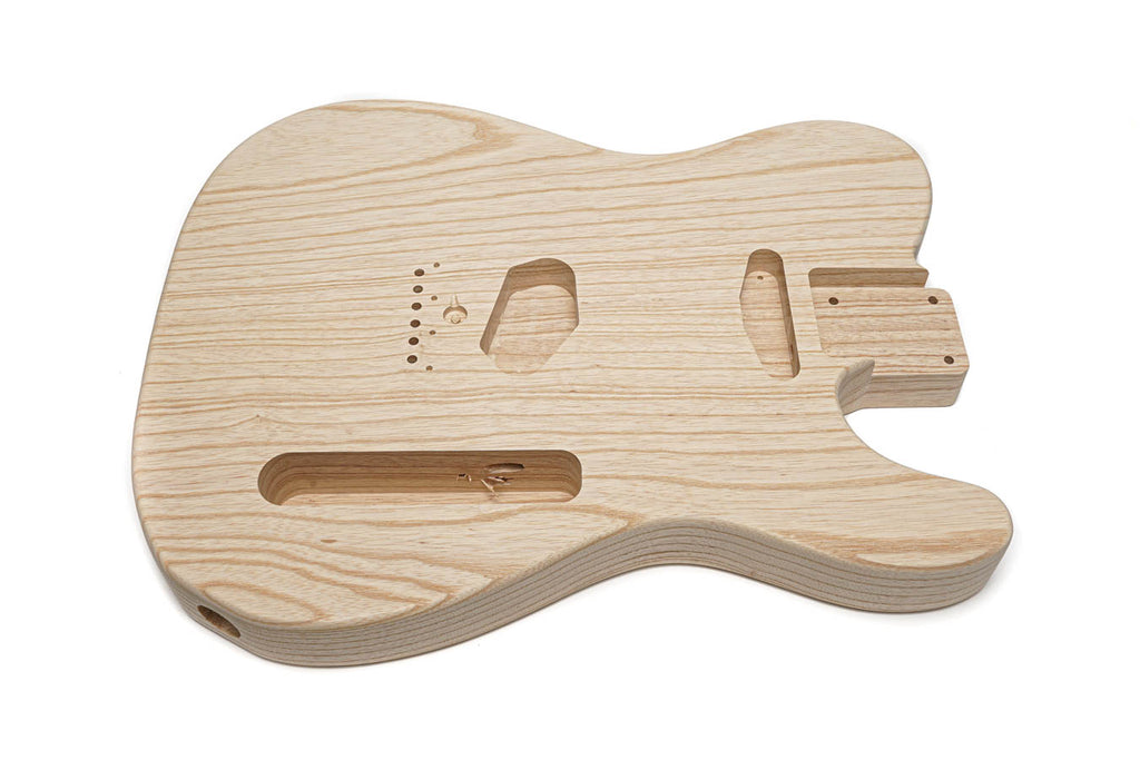Unfinished natural wood guitar body with multiple routed cavities for pickups and controls.