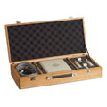 Open wooden case containing two beige microphones, a grey cable, and a manual.