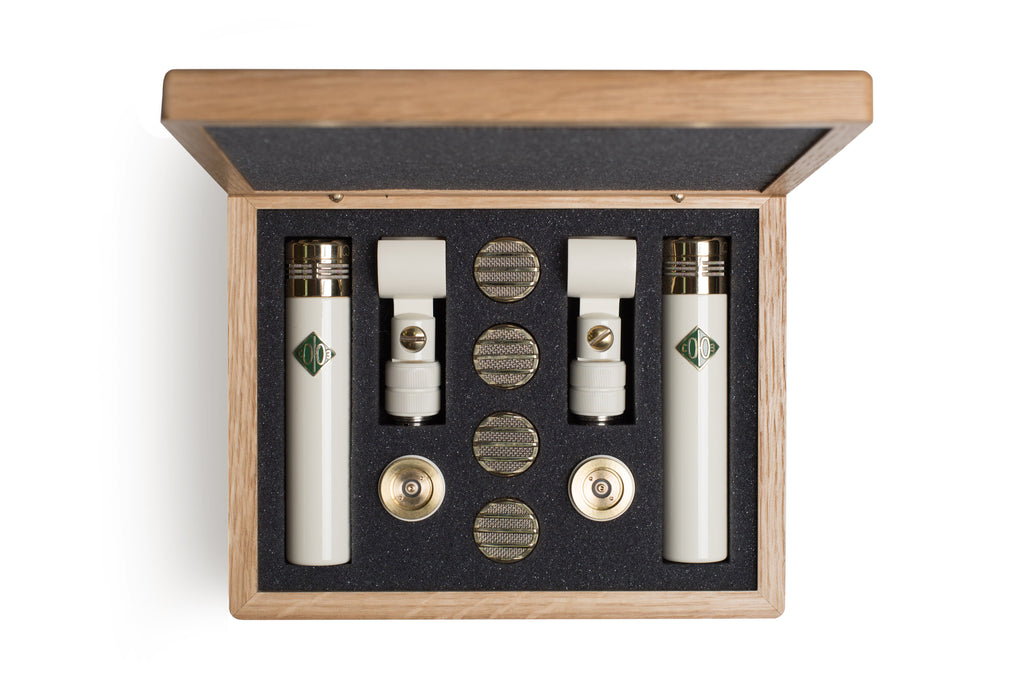 Open wooden case containing two white microphones, two clips, and four round metal capsules on black foam