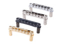 Four metallic guitar bridge saddles with posts, in gold, black, chrome, and silver finishes arranged diagonally.