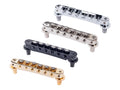 Four metal guitar bridge pieces in silver, chrome, black, and gold arranged diagonally on white background