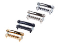 Four guitar bridges and tailpieces in silver, gold, and black finishes arranged in a diagonal pattern.