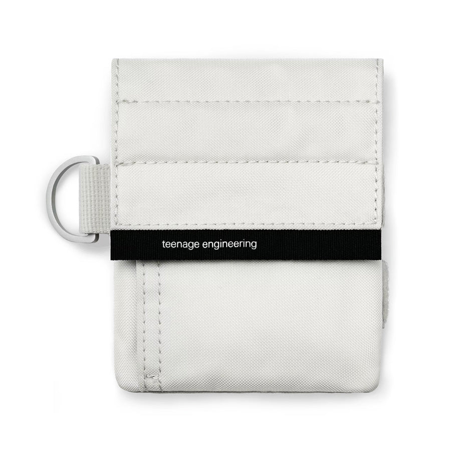 Small white fabric bag with black horizontal band labeled 'teenage engineering' and a metal ring on the side.