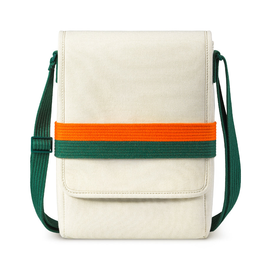 Cream fabric shoulder bag with a front flap and a wide orange and green horizontal band, plus an adjustable green strap.