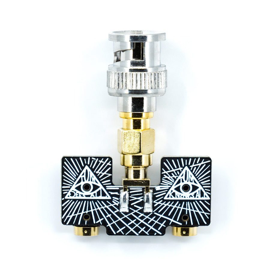 Black adapter with two RCA connectors and a BNC connector mounted on top with white triangular designs.