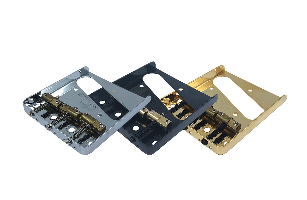 Three metal ashtray-style guitar bridges with brass saddles in silver, black, and gold finishes.