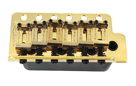 Gold-colored metal guitar bridge component with six string saddles and adjustment screws.