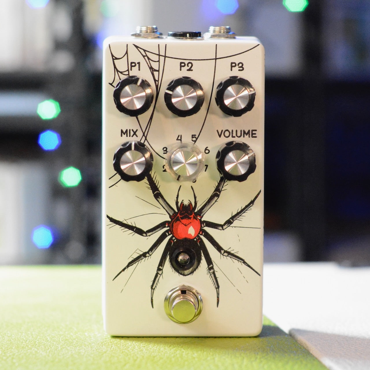 White rectangular guitar effects pedal with black spider graphic and six control knobs plus one footswitch button.