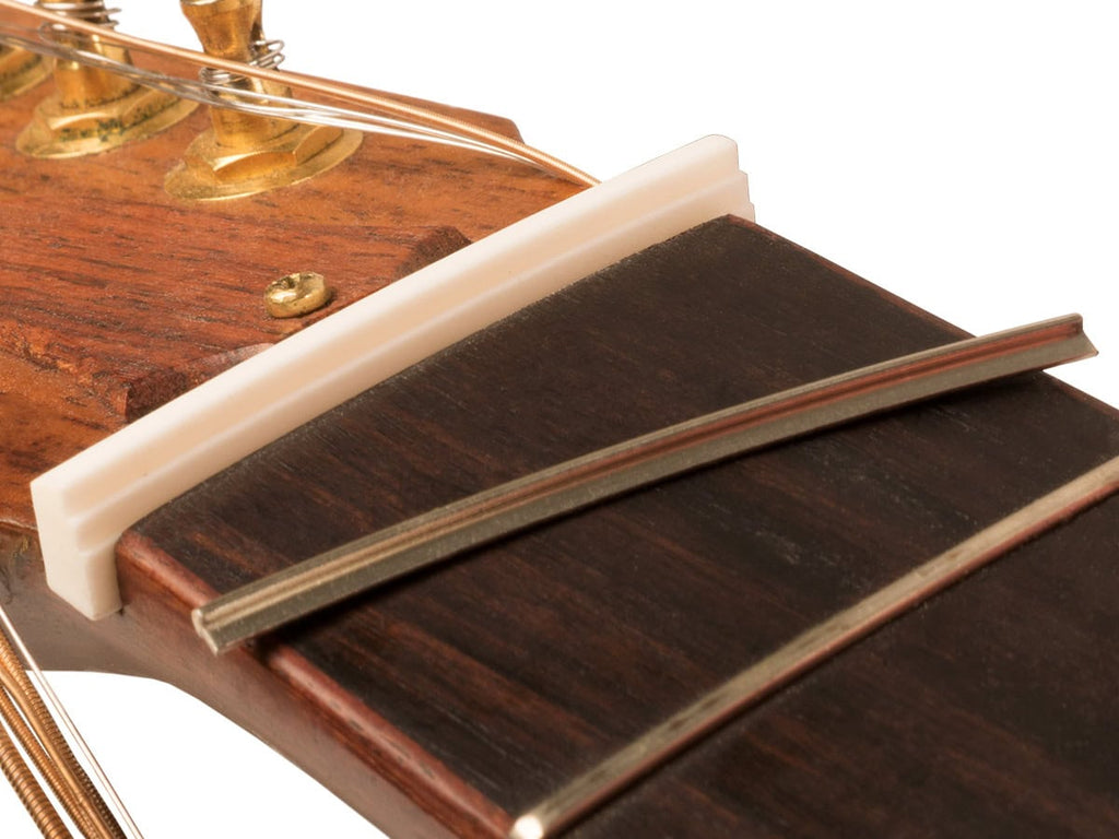 Close-up of a guitar headstock showing a white unslotted nut with strings attached, wood fretboard, and tuning pegs.