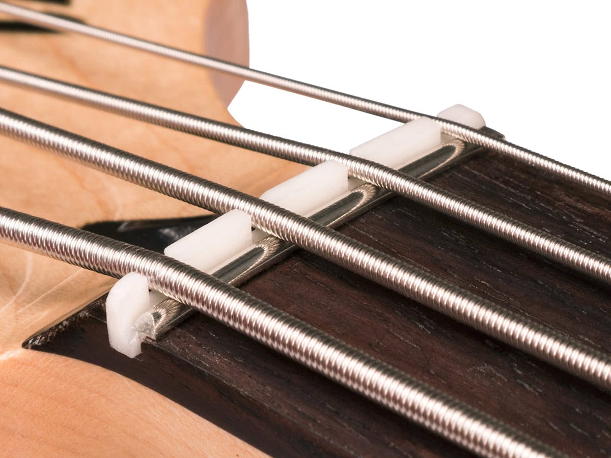 Close-up of a slotted white nut on a guitar neck with four metal strings.