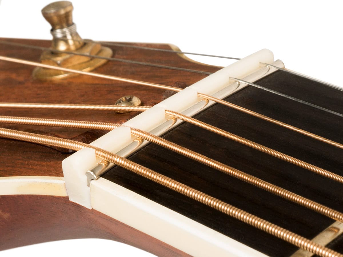 Close-up of acoustic guitar headstock showing white slotted nut with strings in slots.