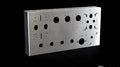 Silver metallic rectangular amplifier chassis with multiple round and oval cutouts on a black background.