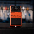 Orange guitar distortion pedal with four black knobs and labeled input and output jacks.