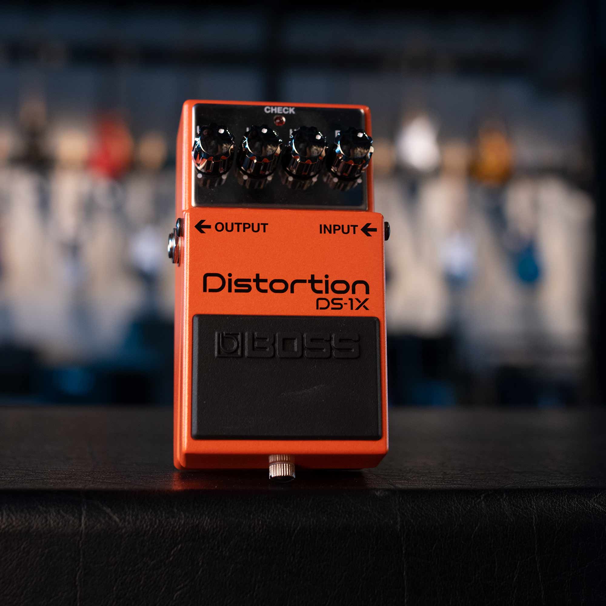 Orange guitar distortion pedal with four black knobs and labeled input and output jacks.