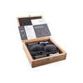 Wooden box opened showing two black microphones, foam windshields, clips, fabric pouches, and papers inside.