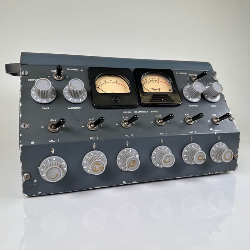 Vintage grey-blue painted steel stereo preamplifier mixer console shown at a three-quarter angle, with two analog VU meters, a top-panel "STEREO PREAMPLIFIER MIXER" legend, a row of small A/B toggle switches, and six large front rotary level knobs labeled MIC 1 through MIC 5 and PHONO.