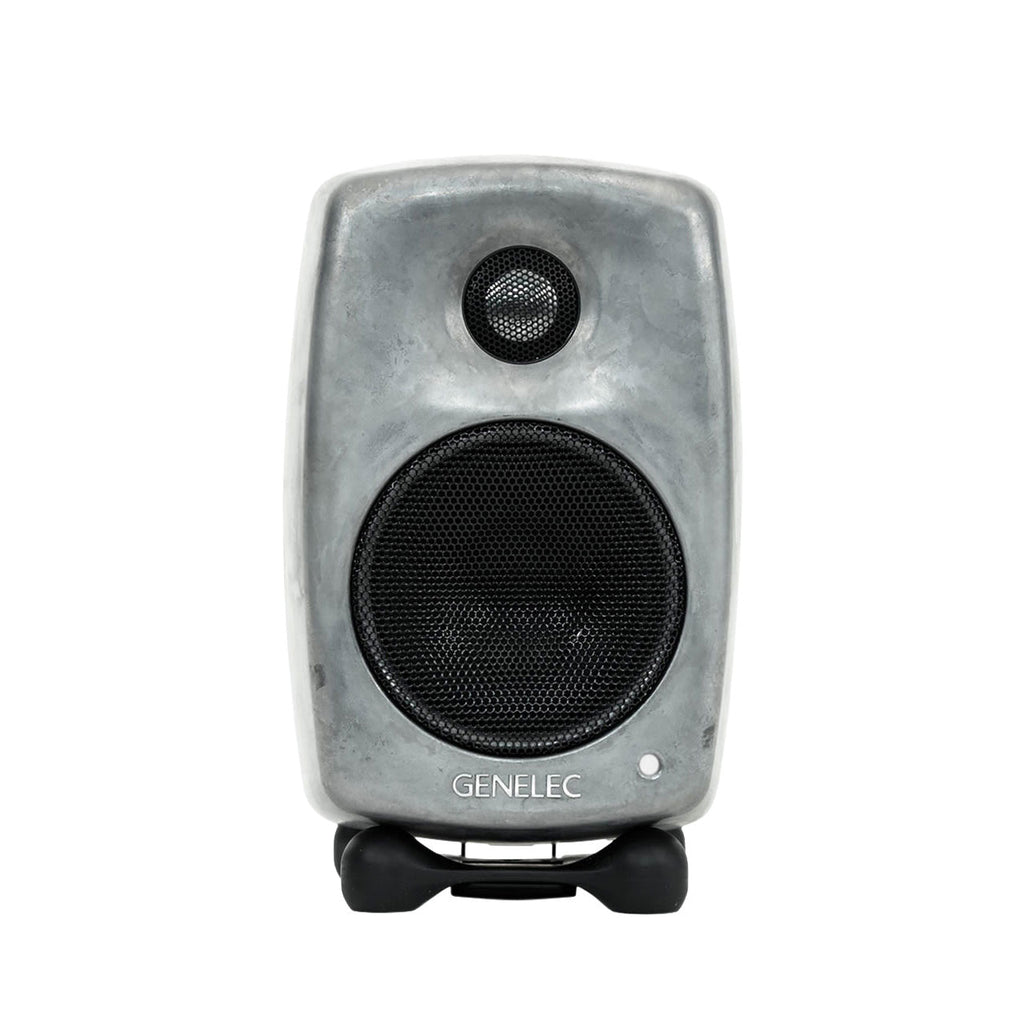 Front view of a compact grey Genelec speaker with protective black speaker grills on two drivers.
