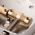 Close-up of brass guitar saddles with adjustment screws mounted on a metallic base plate.