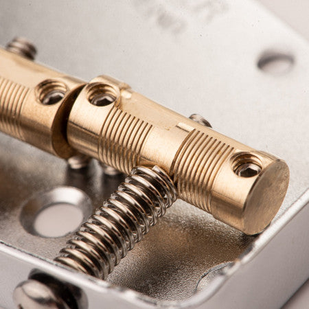 Close-up of brass guitar saddles with adjustment screws mounted on a metallic base plate.