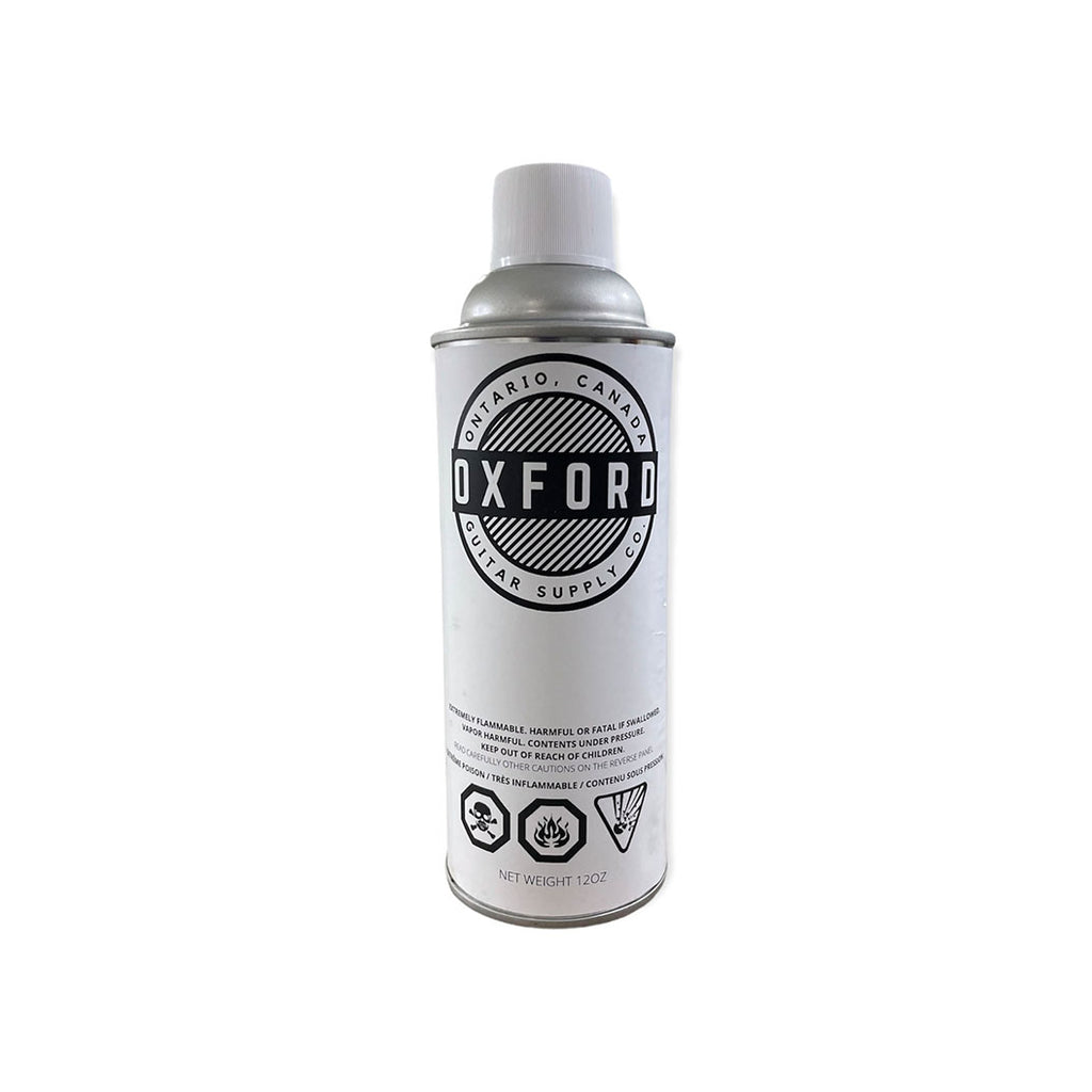 A white and silver aerosol spray can labeled Oxford Guitar Supply Co with safety symbols and warnings.
